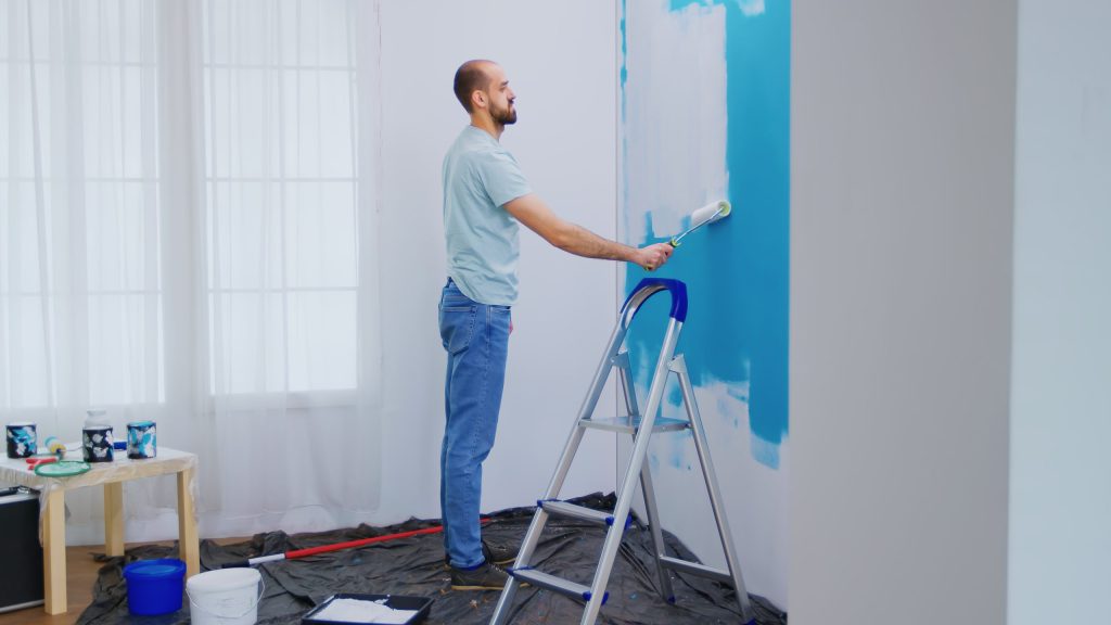Handyman painting wall with roller brush dipped in white paint handyman renovating apartment redecoration and home construction while renovating and improving repair and decorating scaled