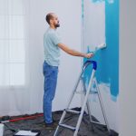 Handyman painting wall with roller brush dipped in white paint handyman renovating apartment redecoration and home construction while renovating and improving repair and decorating scaled